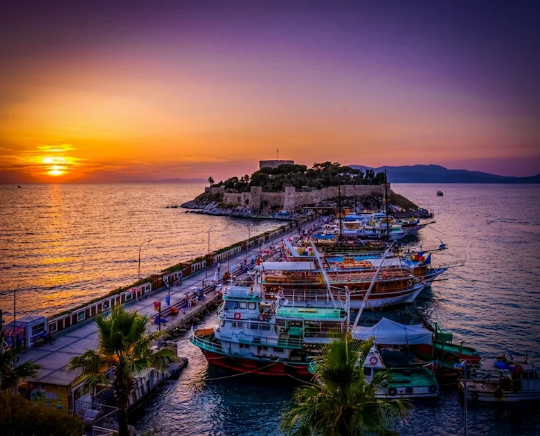 İzmir Havalimanı transferiyle ulaşılan Kuşadası Güvercin Adası'nın günbatımı manzarası, köprü ve teknelerle